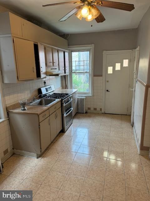 kitchen featuring ceiling fan, radiator heating unit, sink, stainless steel range with gas cooktop, and light tile patterned flooring