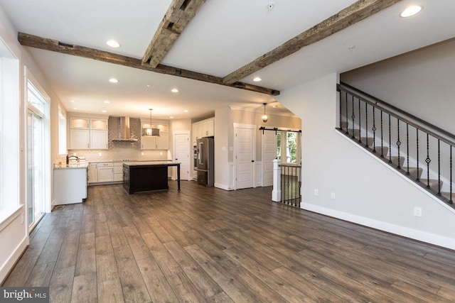 unfurnished living room with a barn door, dark hardwood / wood-style floors, and beam ceiling