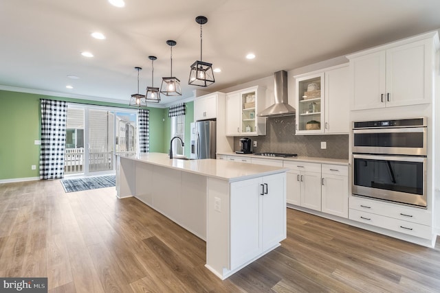 kitchen with a kitchen island with sink, light hardwood / wood-style floors, wall chimney exhaust hood, and stainless steel appliances