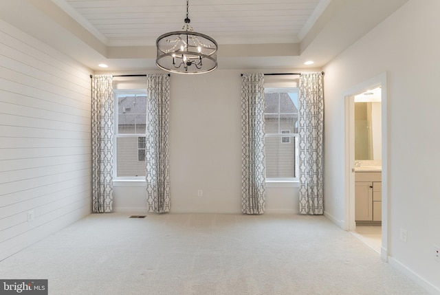 spare room featuring a chandelier, a raised ceiling, and light colored carpet