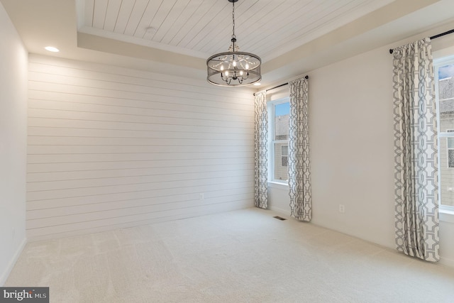 carpeted spare room with an inviting chandelier, a healthy amount of sunlight, and a tray ceiling