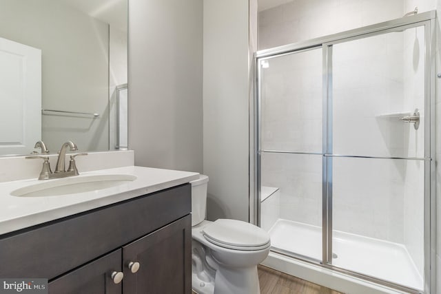 bathroom with toilet, vanity with extensive cabinet space, hardwood / wood-style floors, and a shower with shower door