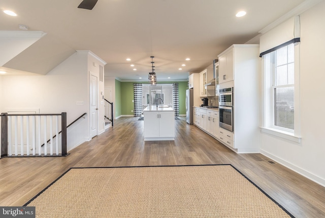 kitchen featuring light hardwood / wood-style floors, white cabinets, an island with sink, stainless steel appliances, and hanging light fixtures