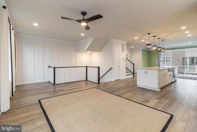 interior space featuring pendant lighting, an island with sink, light hardwood / wood-style floors, ceiling fan with notable chandelier, and white cabinets