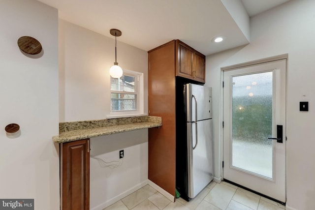 kitchen featuring hanging light fixtures, stainless steel fridge, light tile floors, and light stone counters