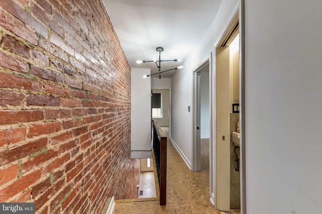 corridor featuring brick wall and a chandelier