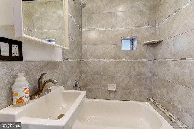 bathroom with tile walls, tiled shower / bath combo, and sink