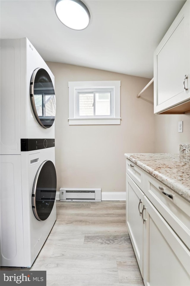 clothes washing area with stacked washer / dryer, cabinets, a baseboard radiator, and light wood-type flooring