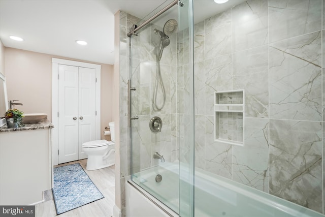 full bathroom featuring sink, bath / shower combo with glass door, wood-type flooring, and toilet