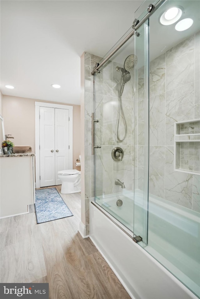 bathroom with hardwood / wood-style flooring, combined bath / shower with glass door, and toilet