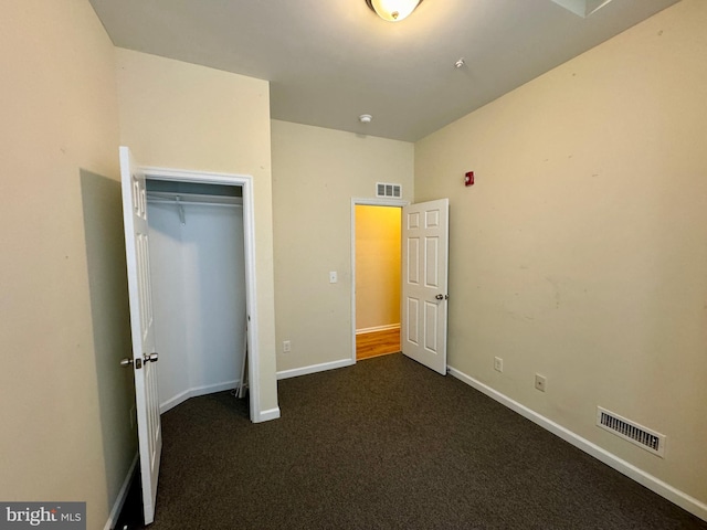 unfurnished bedroom with dark colored carpet and a closet