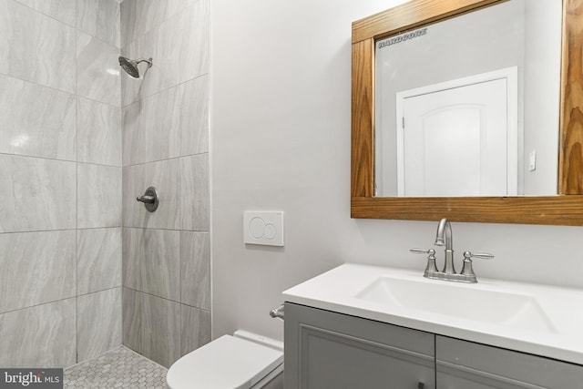 bathroom featuring toilet, a tile shower, and large vanity