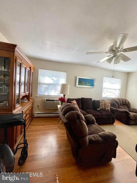 living room with ceiling fan, light hardwood / wood-style flooring, a wall unit AC, and a baseboard radiator