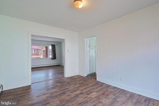 unfurnished room featuring baseboard heating and dark hardwood / wood-style floors