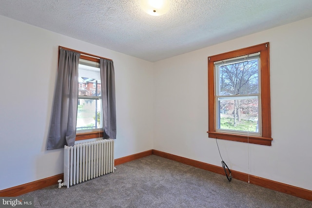 empty room featuring a textured ceiling, radiator, and dark colored carpet