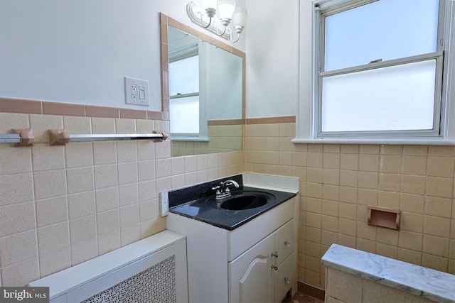 bathroom featuring a chandelier, backsplash, radiator heating unit, vanity with extensive cabinet space, and tile walls