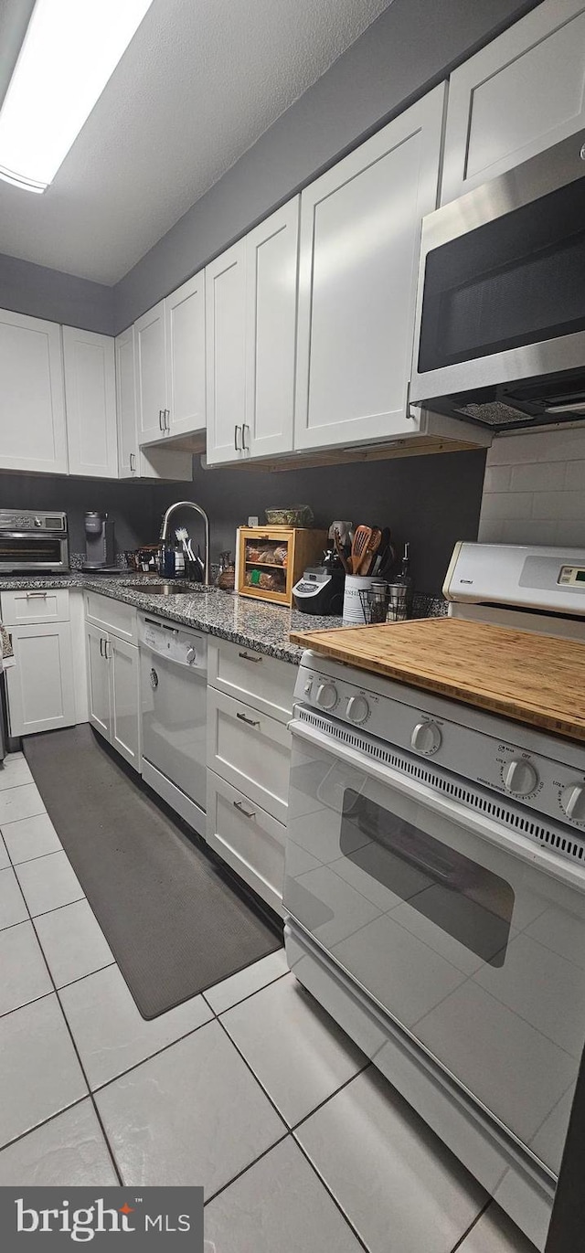 kitchen with light tile floors, range, white dishwasher, and white cabinetry