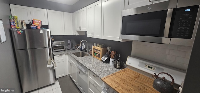 kitchen with stainless steel appliances, light tile floors, light stone countertops, white cabinetry, and sink