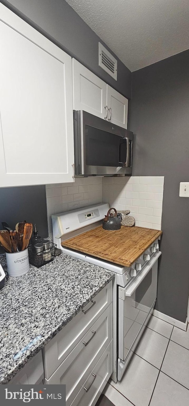 kitchen featuring light tile flooring, tasteful backsplash, appliances with stainless steel finishes, white cabinets, and light stone counters