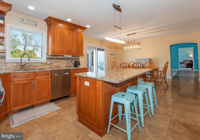 kitchen with a breakfast bar, a center island, sink, hanging light fixtures, and stainless steel dishwasher