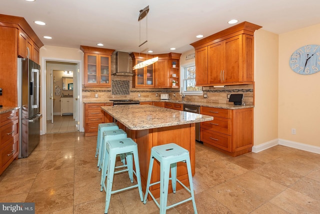 kitchen with wall chimney range hood, decorative light fixtures, a kitchen island, a kitchen bar, and stainless steel appliances