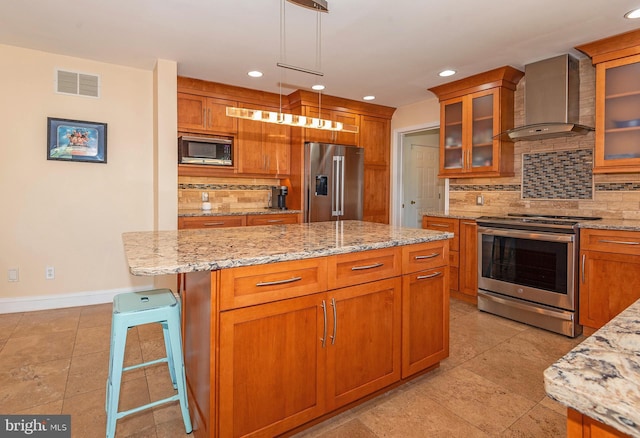 kitchen featuring pendant lighting, wall chimney range hood, a kitchen island, a kitchen bar, and stainless steel appliances