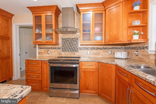 kitchen with stainless steel electric range, sink, wall chimney exhaust hood, tasteful backsplash, and light stone counters