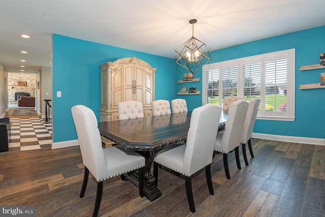 dining area featuring a stone fireplace, dark wood-type flooring, and an inviting chandelier