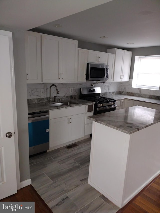 kitchen with light stone counters, white cabinetry, stainless steel appliances, backsplash, and sink