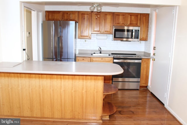 kitchen with appliances with stainless steel finishes, ceiling fan, backsplash, dark hardwood / wood-style flooring, and sink