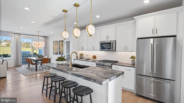 kitchen with an island with sink, white cabinets, appliances with stainless steel finishes, tasteful backsplash, and decorative light fixtures