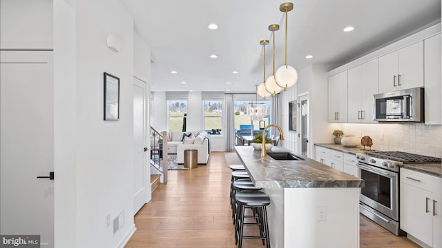 kitchen featuring stainless steel appliances, decorative light fixtures, a center island with sink, white cabinets, and sink