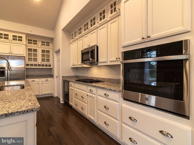 kitchen with dark hardwood / wood-style flooring, white cabinetry, appliances with stainless steel finishes, vaulted ceiling, and light stone counters