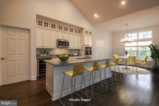 kitchen with high vaulted ceiling, light stone countertops, decorative light fixtures, a center island with sink, and dark hardwood / wood-style floors