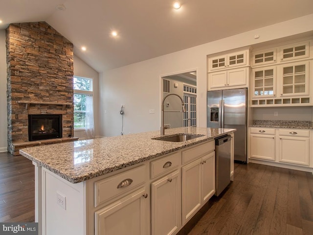 kitchen featuring a kitchen island with sink, dark hardwood / wood-style flooring, stainless steel dishwasher, sink, and a stone fireplace