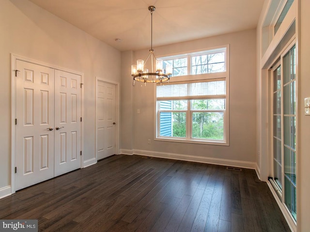 spare room featuring dark wood-type flooring and a notable chandelier