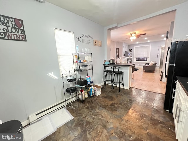 kitchen with white cabinetry, ceiling fan, a kitchen breakfast bar, a baseboard radiator, and dark tile flooring