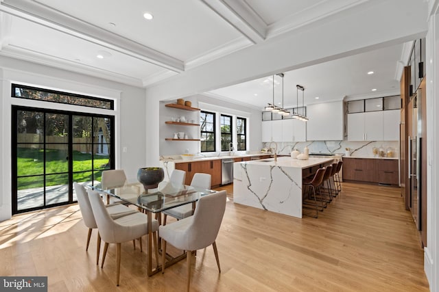 dining area featuring beam ceiling, crown molding, sink, and light wood-type flooring