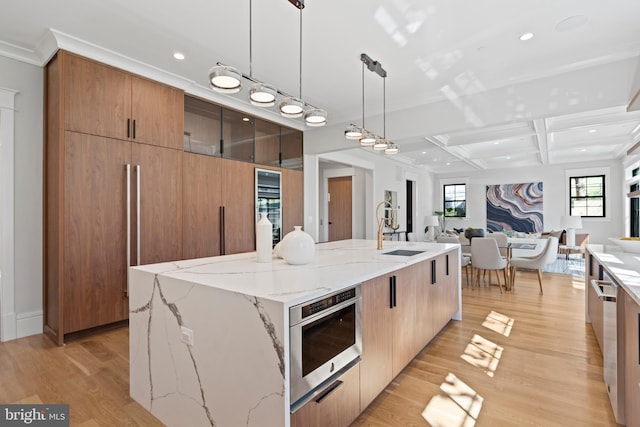 kitchen with appliances with stainless steel finishes, a center island with sink, coffered ceiling, and light wood-type flooring