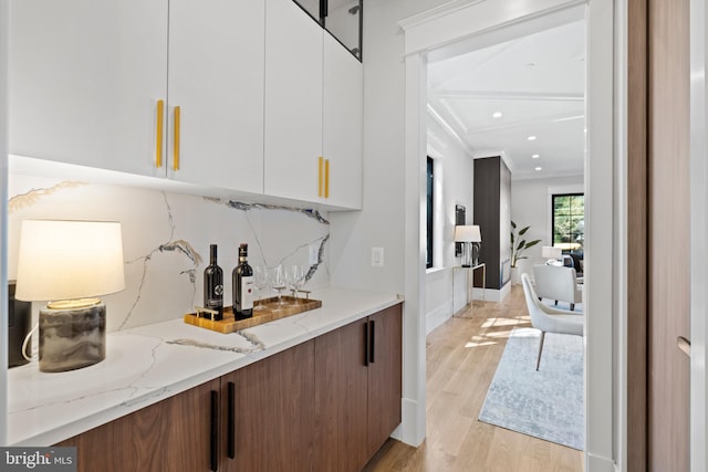 bar featuring white cabinetry, ornamental molding, light stone counters, and light hardwood / wood-style floors