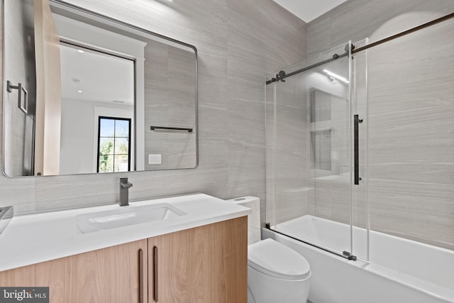 full bathroom featuring tile walls, combined bath / shower with glass door, toilet, and vanity