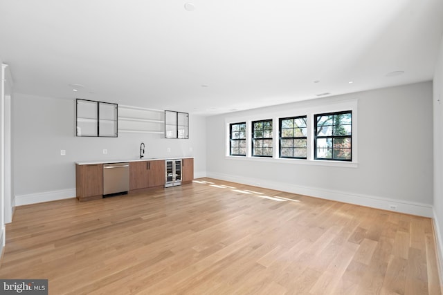 unfurnished living room with beverage cooler, light hardwood / wood-style floors, and sink