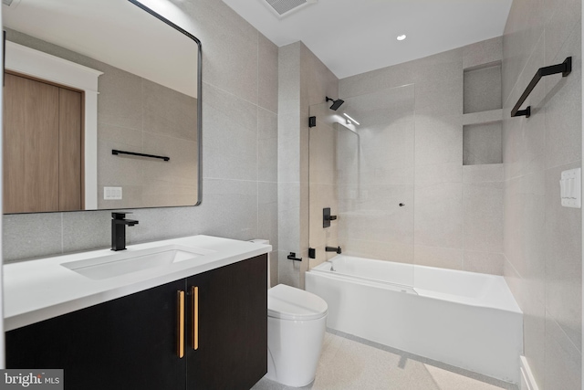 full bathroom featuring tiled shower / bath, toilet, vanity, and tile walls