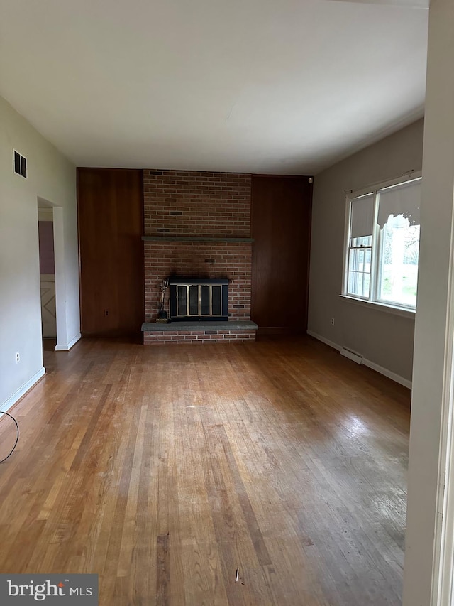 unfurnished living room featuring hardwood / wood-style flooring, a baseboard heating unit, brick wall, and a fireplace