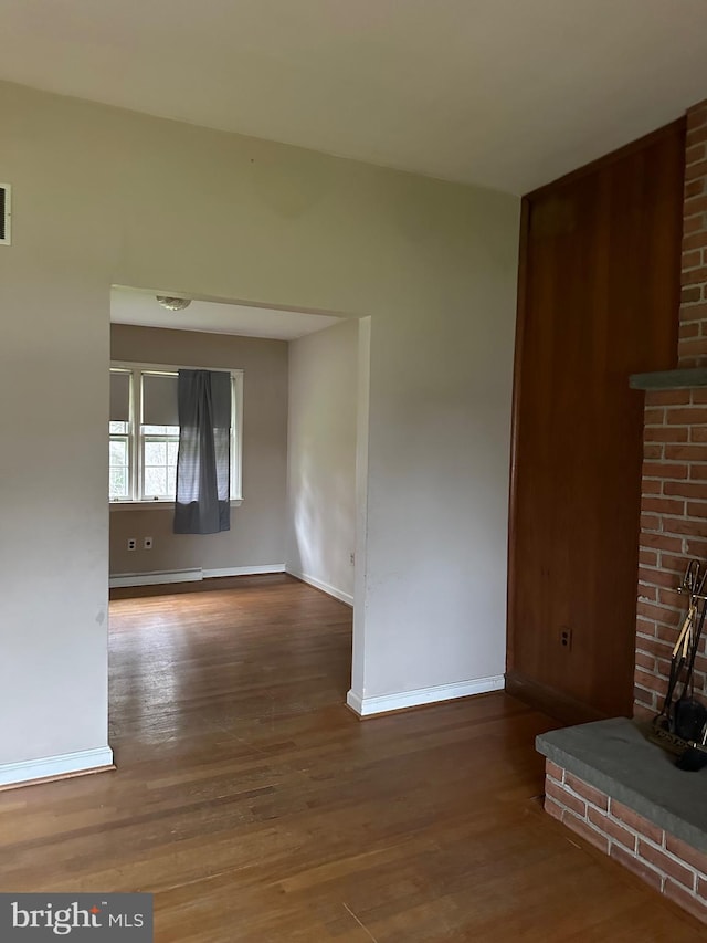 unfurnished living room featuring brick wall, a baseboard heating unit, and dark hardwood / wood-style flooring