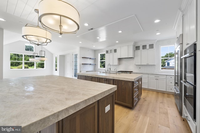 kitchen featuring a kitchen island with sink, hanging light fixtures, white cabinets, light hardwood / wood-style flooring, and backsplash