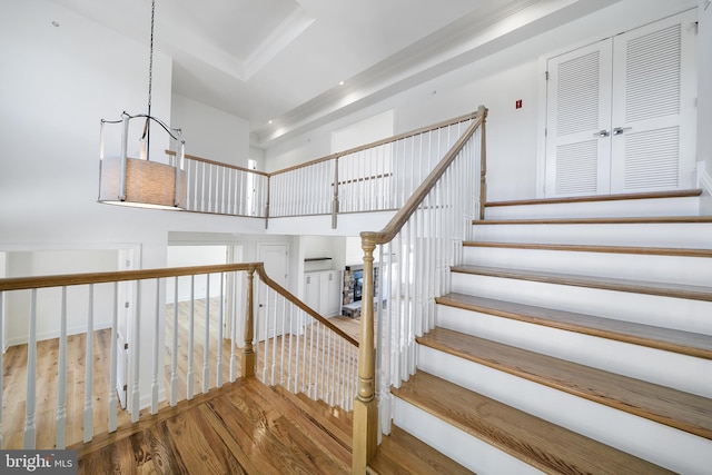 staircase featuring a notable chandelier, wood-type flooring, and a raised ceiling