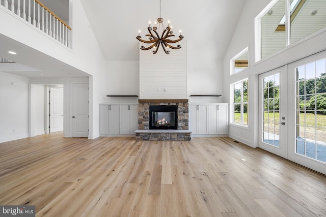 unfurnished living room featuring light hardwood / wood-style floors, a notable chandelier, high vaulted ceiling, french doors, and a stone fireplace