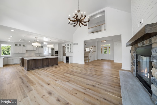 unfurnished living room featuring light hardwood / wood-style floors, a stone fireplace, a chandelier, and a towering ceiling