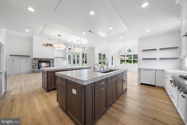 kitchen with an island with sink, white cabinets, light hardwood / wood-style flooring, a fireplace, and decorative light fixtures